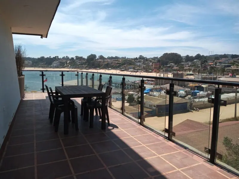 Une table et des chaises sont disposées sur une terrasse carrelée avec vue sur la mer et la côte.