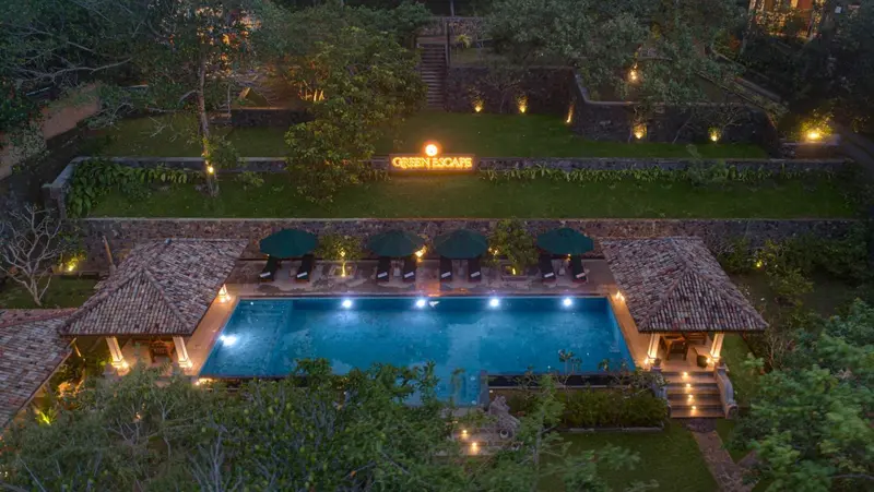 Vue aérienne d'une piscine illuminée dans un jardin soigné.