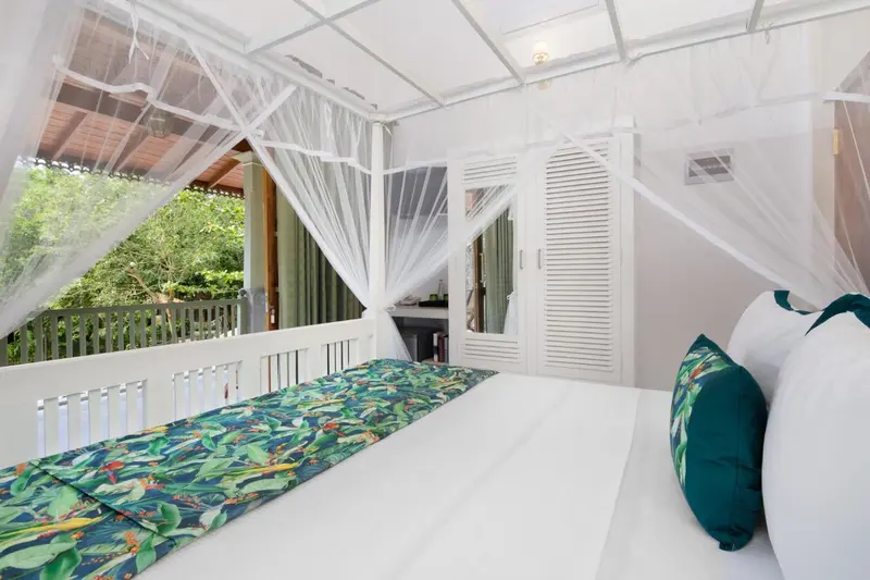 Une chambre lumineuse avec un lit recouvert d'une moustiquaire et vue sur la végétation.