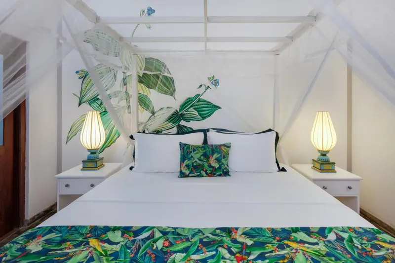 Lit à baldaquin blanc dans une chambre décorée de motifs tropicaux.