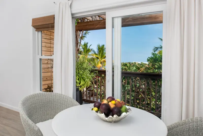 Une table ronde avec des fruits frais est placée devant une baie vitrée donnant sur une végétation luxuriante.
