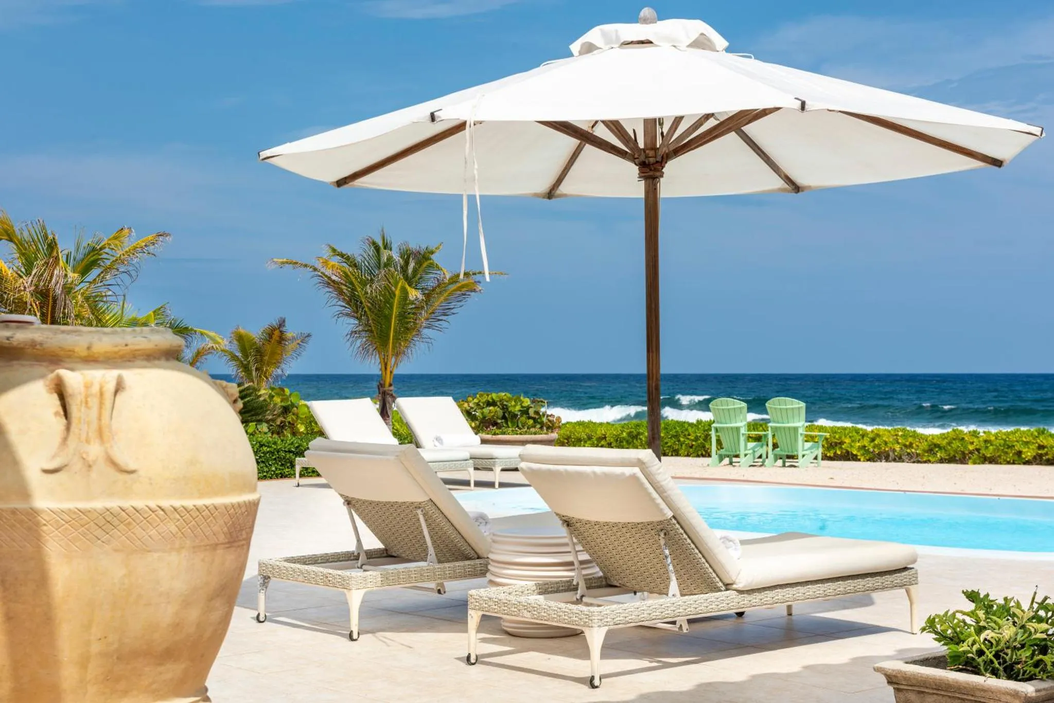 Transats blancs disposés autour d'une piscine avec vue sur la mer.