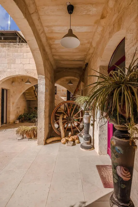 Une galerie voûtée mène à une cour intérieure décorée d'une roue de charrette et de plantes.