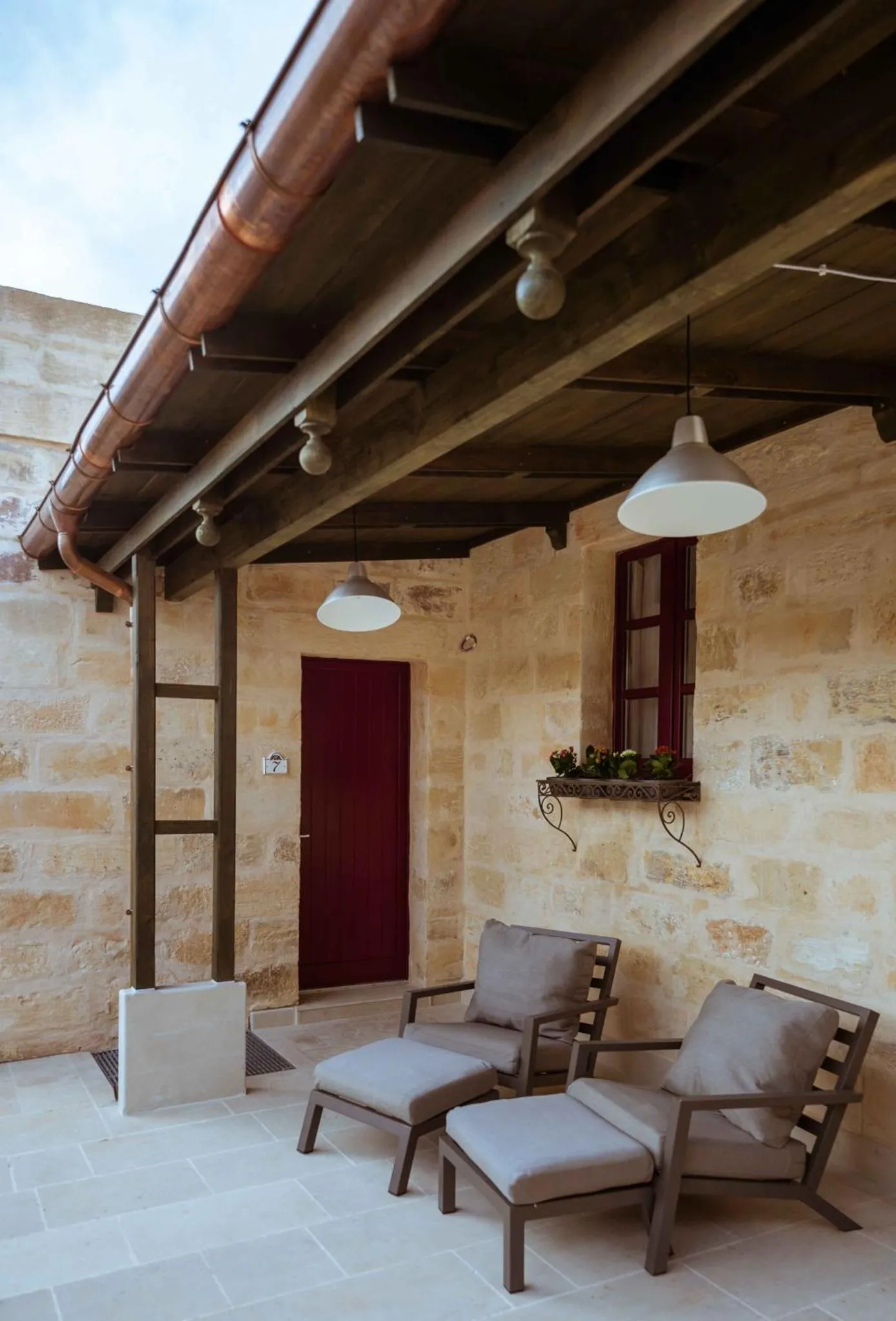 Terrasse ombragée avec deux fauteuils et une porte rouge.