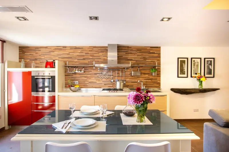 Une cuisine moderne s'ouvre sur une table à manger avec des chaises blanches.
