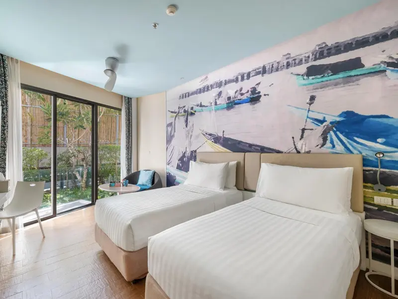 Chambre lumineuse avec deux lits simples et une grande fresque murale représentant des bateaux.