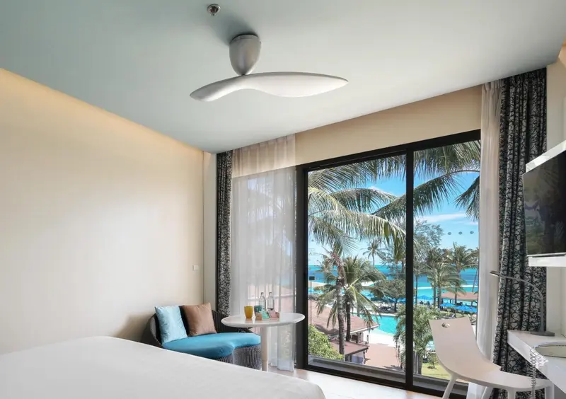 Une chambre lumineuse avec vue sur la végétation et la mer.