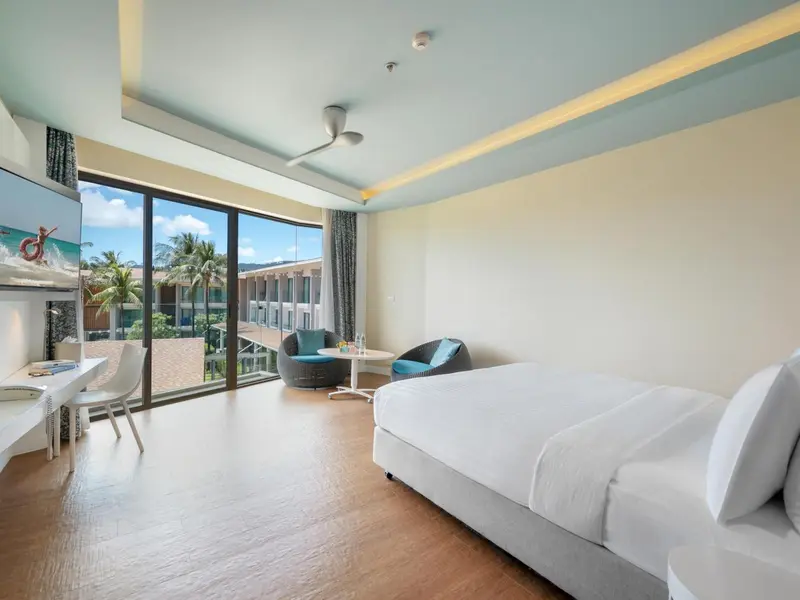 Chambre lumineuse avec un grand lit et un coin salon donnant sur une vue extérieure.