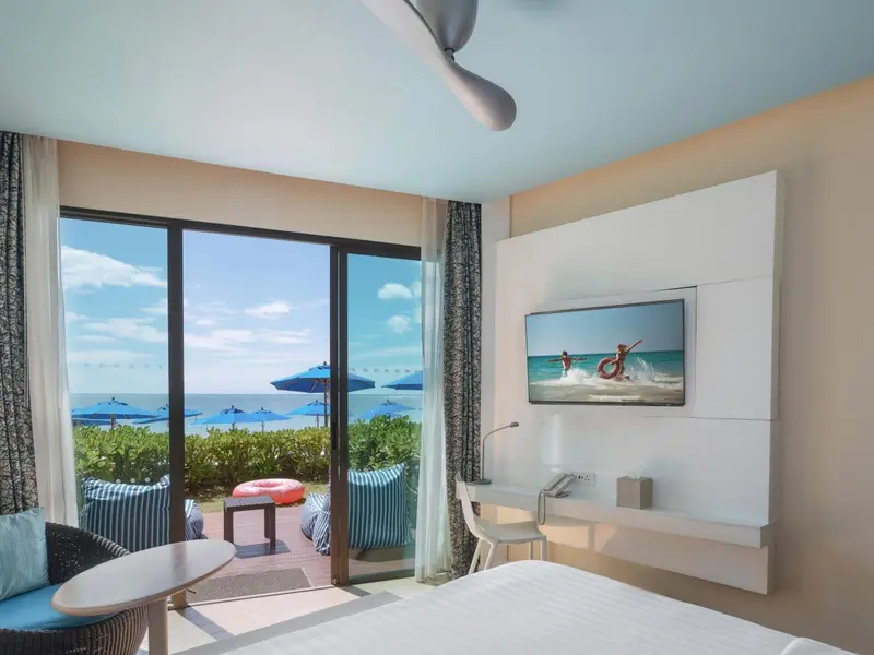 Une chambre lumineuse donne sur une plage avec des parasols bleus.