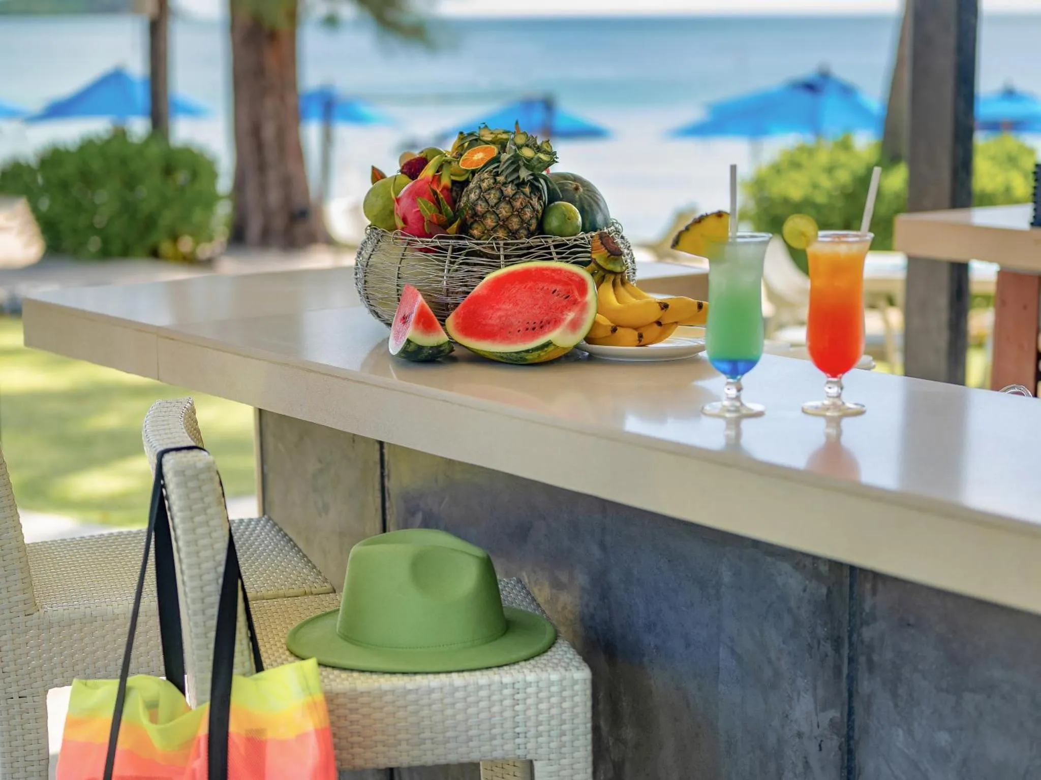 Une table blanche présente des fruits frais et des boissons colorées sur une pelouse verte.