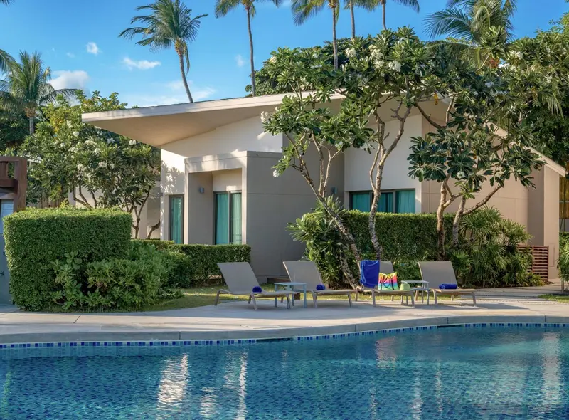 Bâtiment blanc entouré de végétation tropicale avec des transats près d'une piscine.