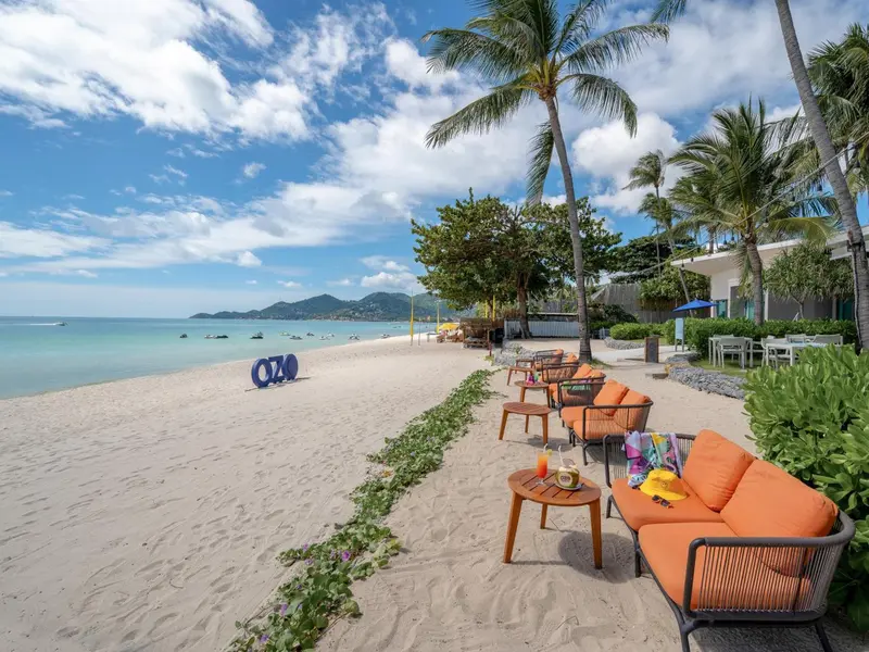 Mobilier de salon orange sur une plage de sable blanc avec des palmiers en arrière-plan.