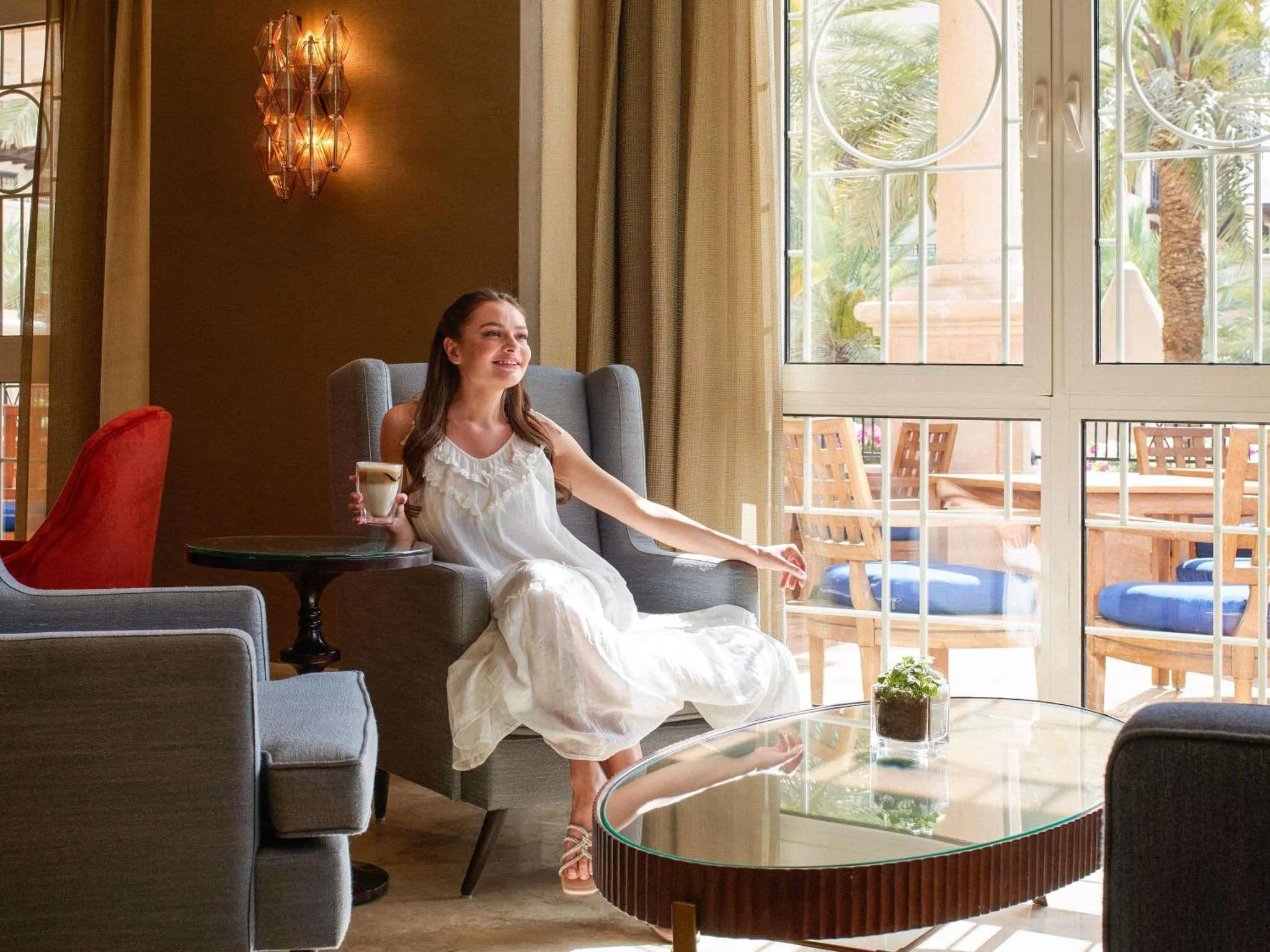 Une femme souriante se détend dans un salon lumineux avec une boisson.