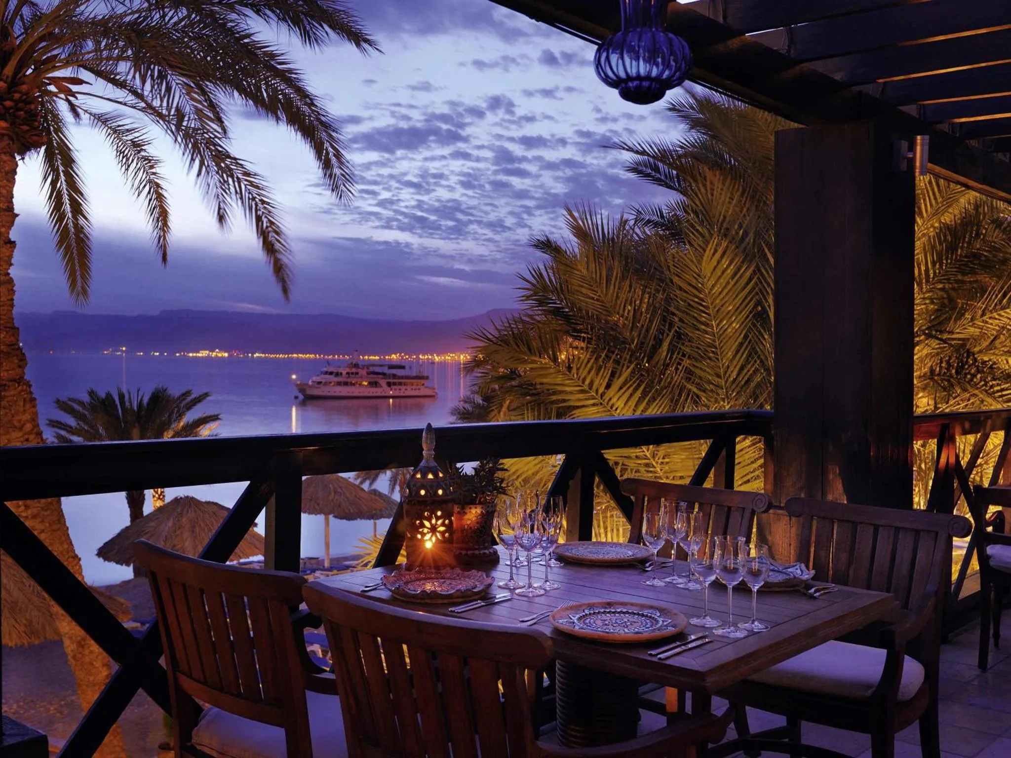 Une table est dressée sur une terrasse avec vue sur la mer au coucher du soleil.