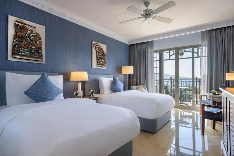 Chambre lumineuse avec deux lits simples et vue sur un paysage verdoyant.
