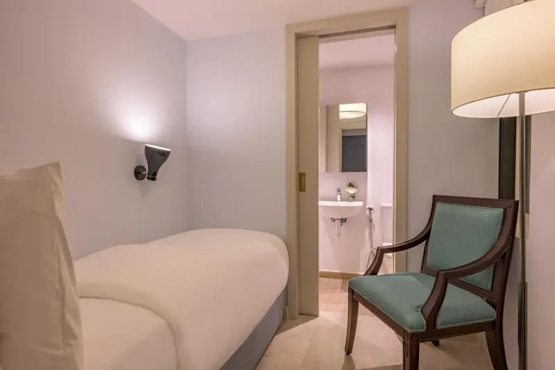 Une chambre lumineuse avec un lit simple et un fauteuil.