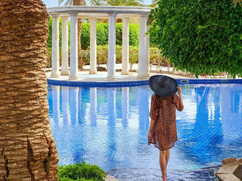 Une personne se tient face à une piscine ornée de colonnes.