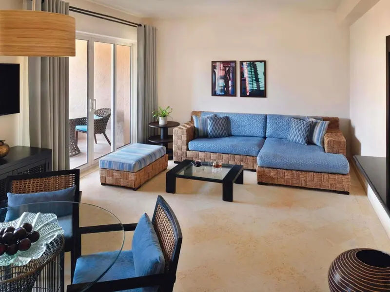 Un salon lumineux avec un canapé d'angle bleu et des fauteuils en osier.