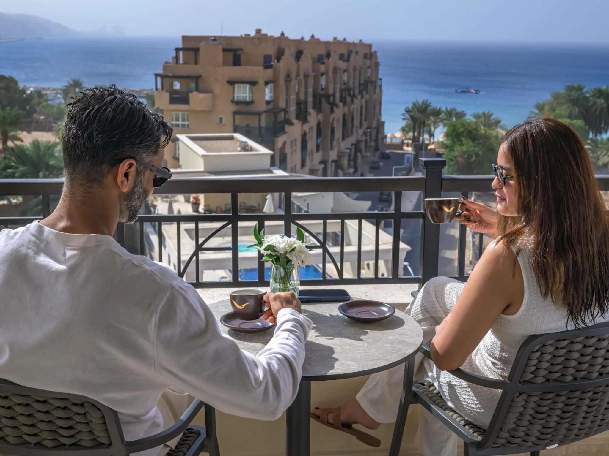 Un couple prend son petit-déjeuner sur une terrasse ensoleillée avec vue sur la mer.