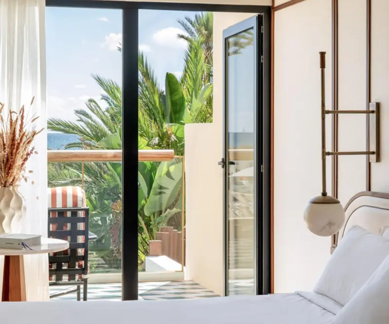 Une chambre lumineuse s'ouvre sur une terrasse avec vue sur la végétation.