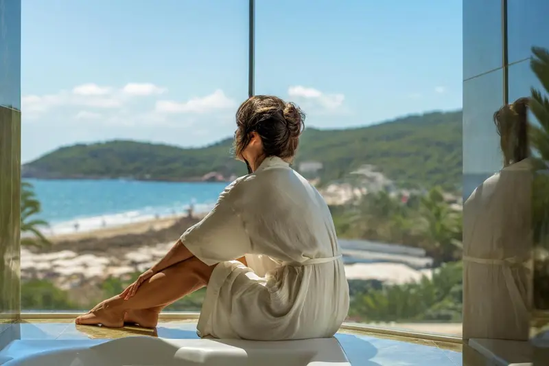 Une femme assise sur le rebord d'une fenêtre contemple la mer.