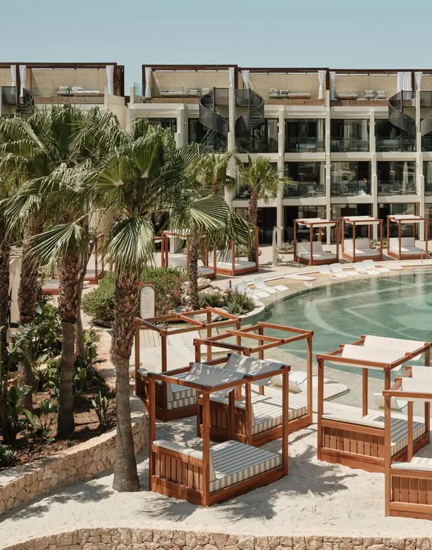 Transats en bois et parasols disposés autour d'une piscine dans un complexe hôtelier.