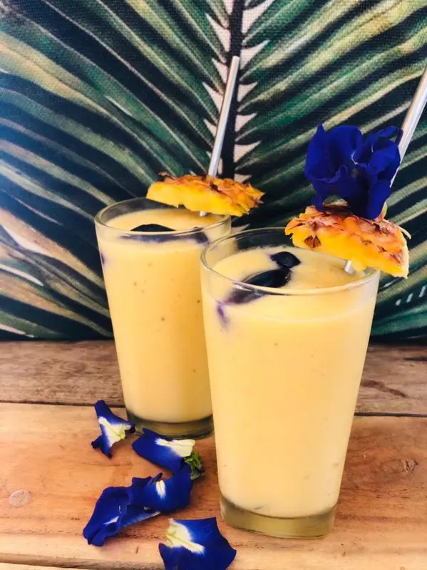 Deux verres de cocktail exotiques décorés de fleurs et d'ananas sur une table en bois.