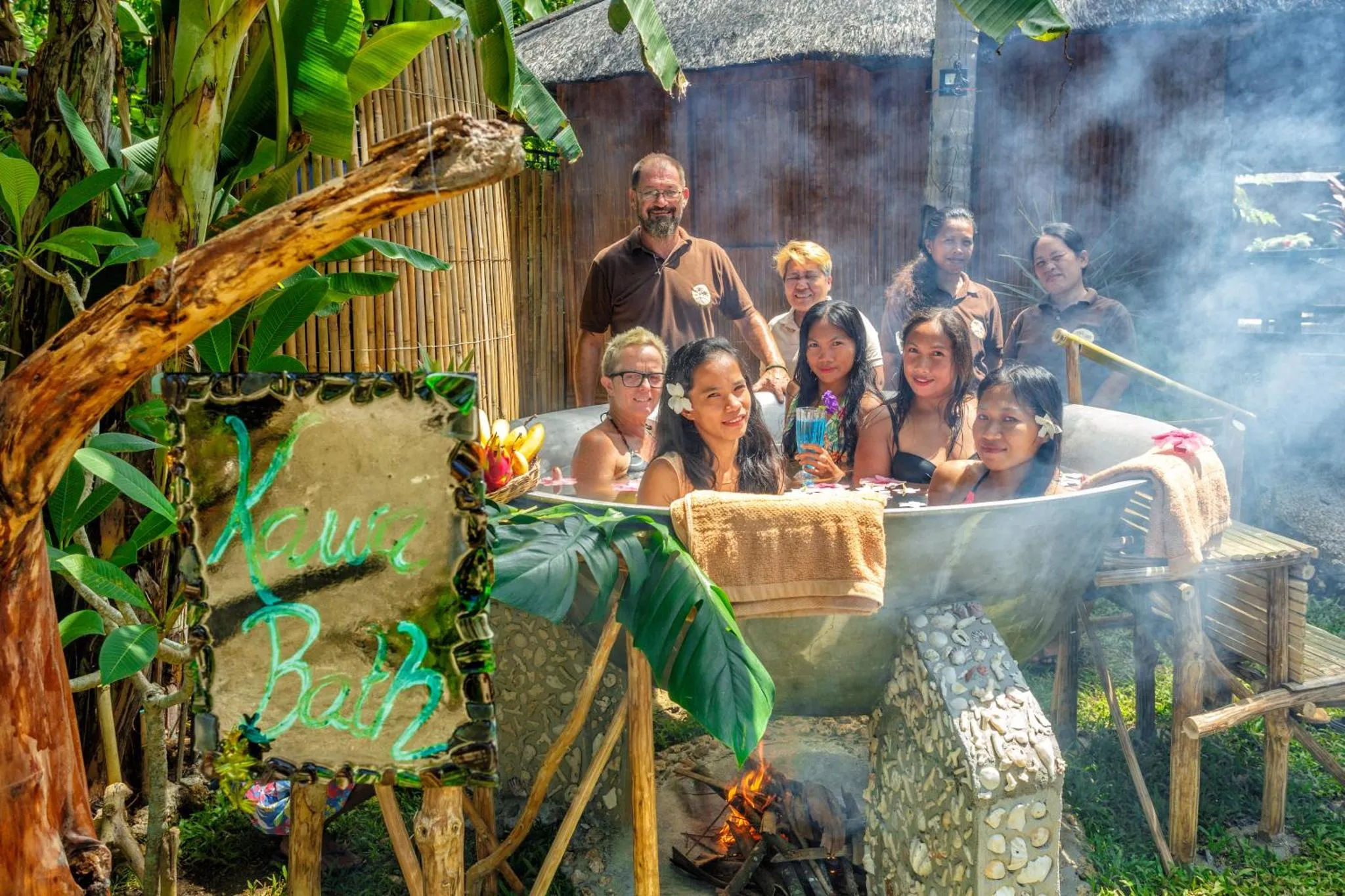 Un groupe de personnes souriantes se détend dans des bains en pierre au milieu d'une végétation luxuriante.