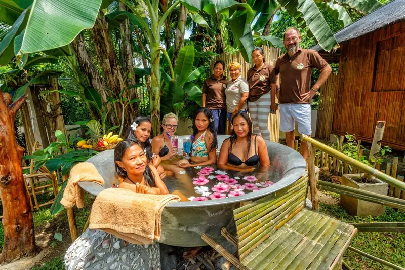 Groupe de personnes souriantes près d'un bain extérieur décoré de fleurs.
