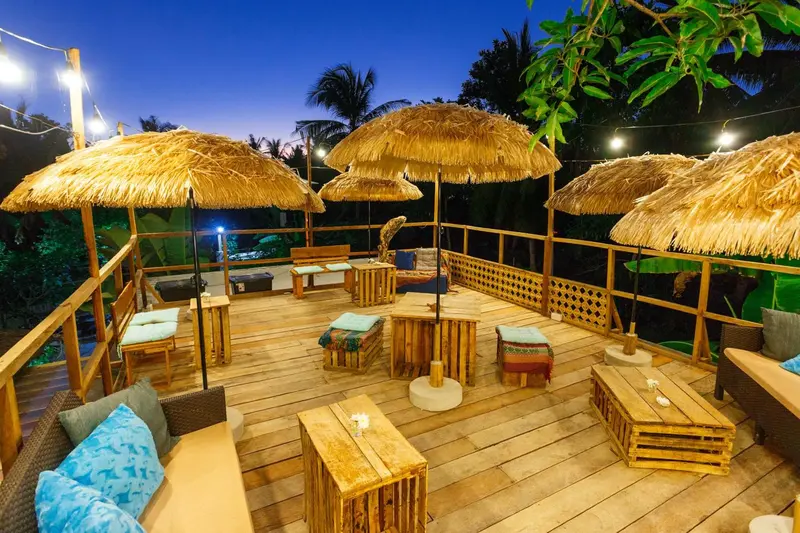 Terrasse en bois avec mobilier d'extérieur et parasols en chaume sous un ciel crépusculaire.