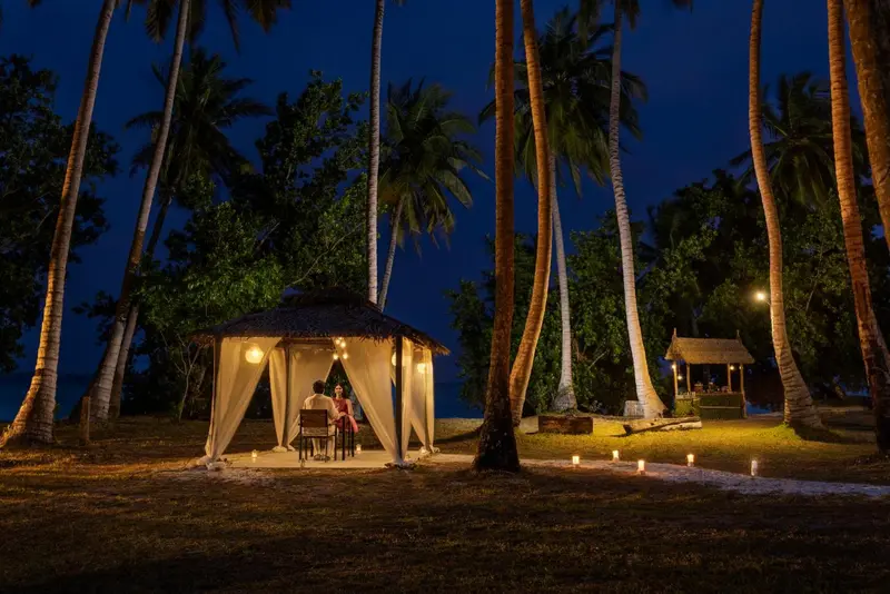 Un couple dîne à une table éclairée par des bougies dans une structure ouverte sur la plage.