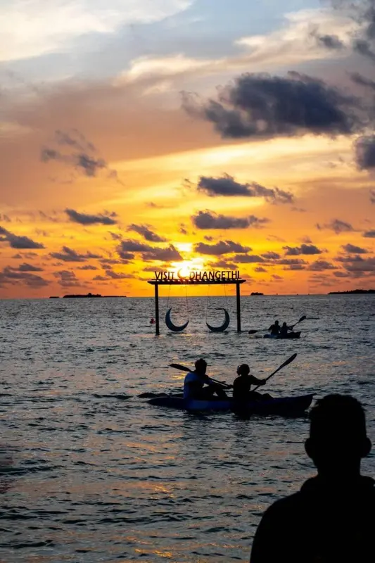 Silhouette de personnes pagayant sur une mer calme au coucher du soleil.