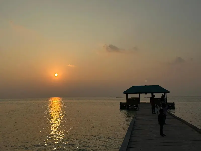 Un ponton en bois s'avance sur une mer calme au coucher du soleil.