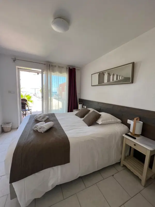 Une chambre lumineuse avec un grand lit recouvert d'une courtepointe blanche et de coussins.