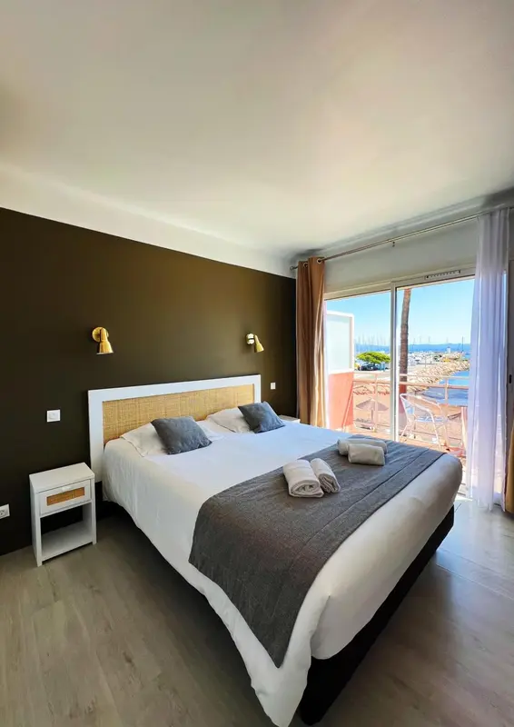 Une chambre lumineuse avec un grand lit et un accès à une terrasse ensoleillée.