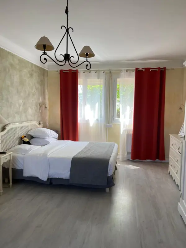 Une chambre lumineuse avec un lit recouvert d'une courtepointe grise et des rideaux rouges.