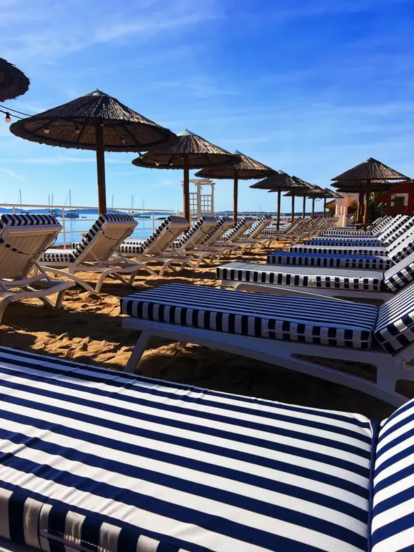 Transats rayés sous des parasols de chaume sur une plage de sable.