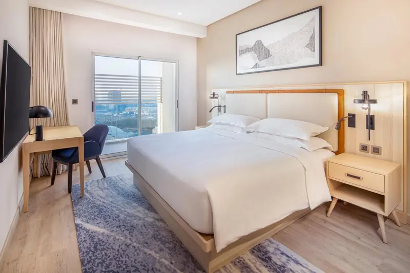 Chambre lumineuse avec un grand lit et un bureau près d'une fenêtre.