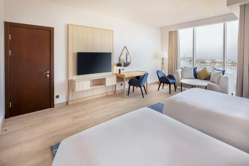 Une chambre lumineuse avec un lit, un coin salon et une vue sur la mer.