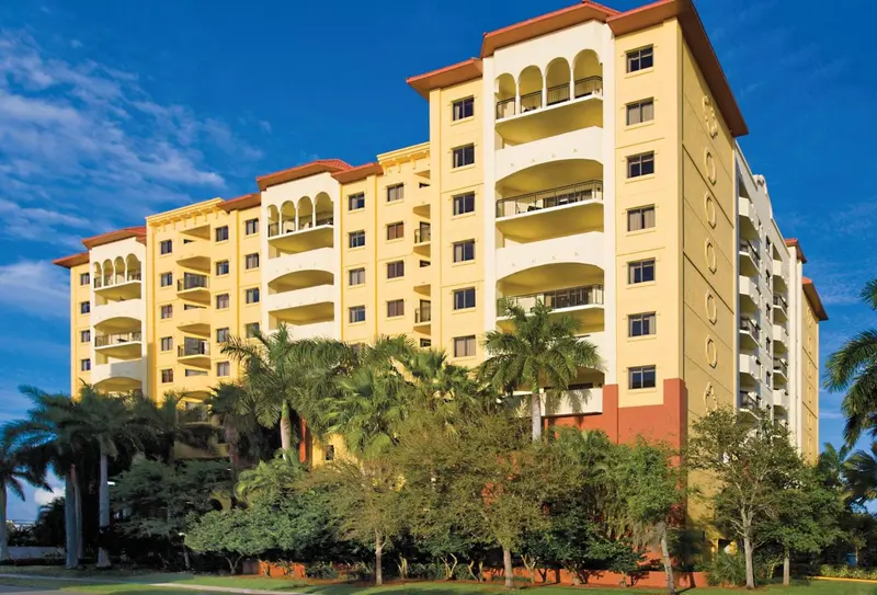 Bâtiment jaune à plusieurs étages avec des balcons et une végétation tropicale.