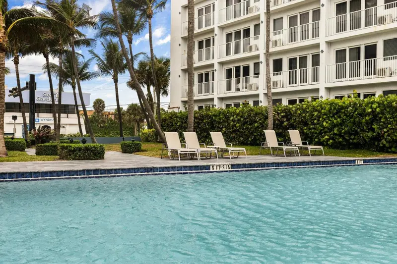 Transats blancs alignés au bord d'une piscine turquoise, devant un bâtiment blanc et des palmiers.