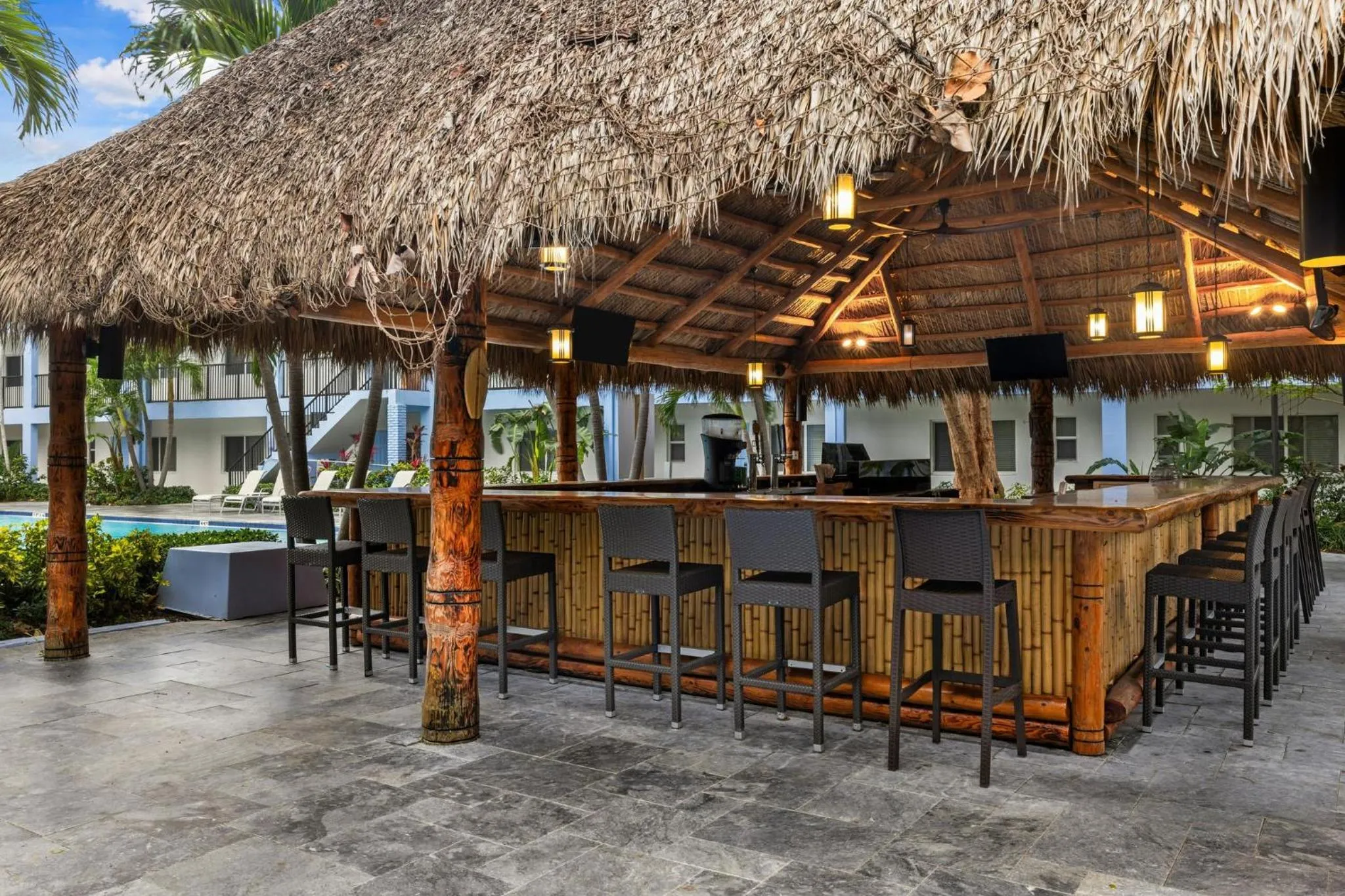 Un bar extérieur en bois avec des tabourets est abrité sous un toit de chaume.