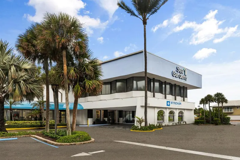 Bâtiment blanc à deux étages entouré de végétation tropicale et d'un parking.