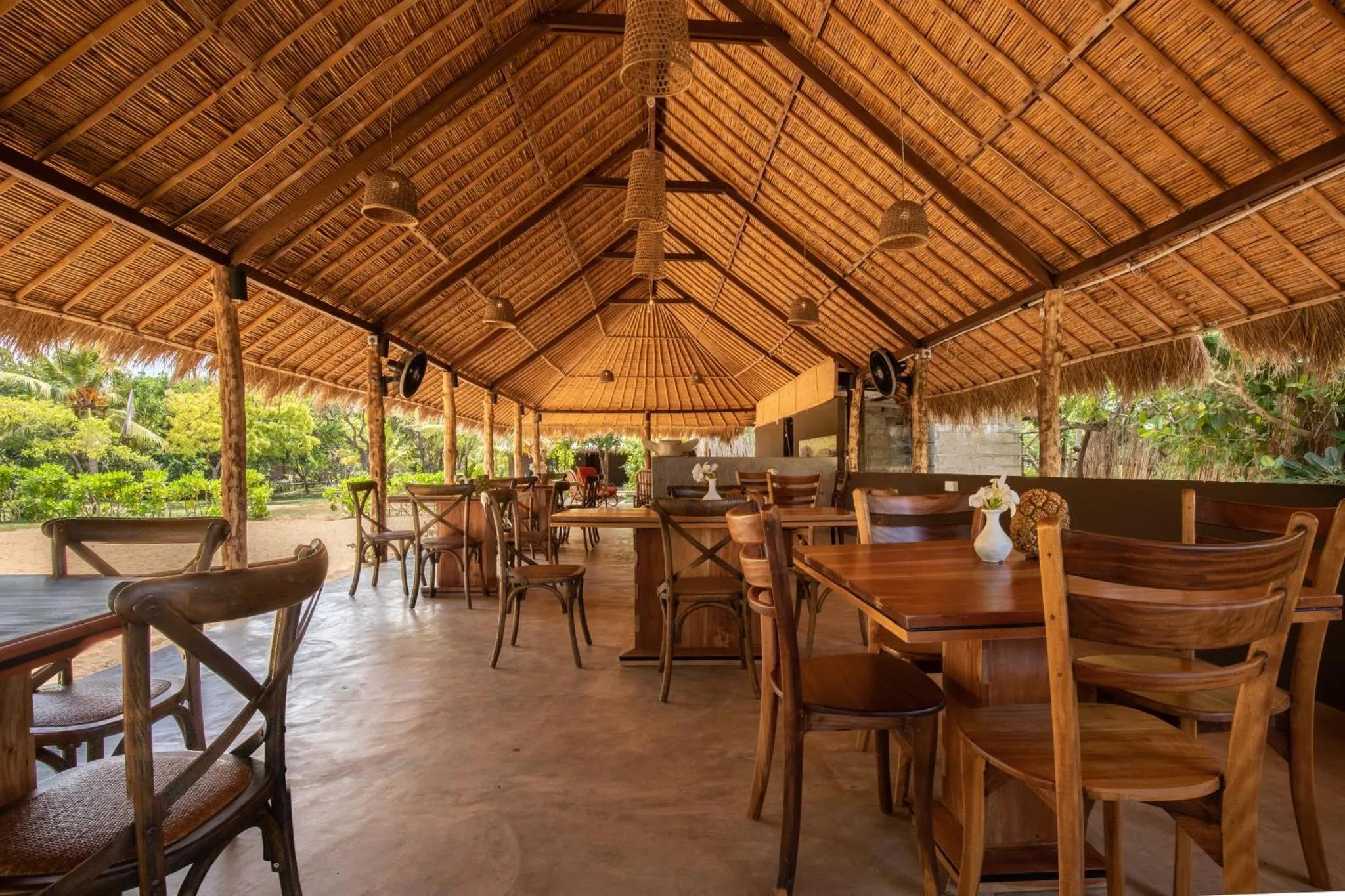 Une salle à manger extérieure avec des tables en bois et un toit de chaume.