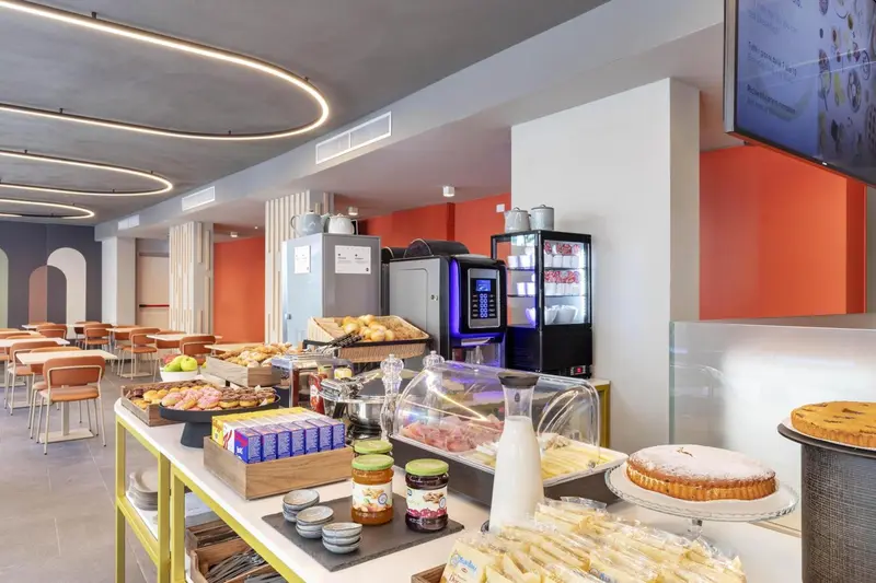 Un buffet propose des viennoiseries, des fruits et des boissons dans une salle lumineuse.