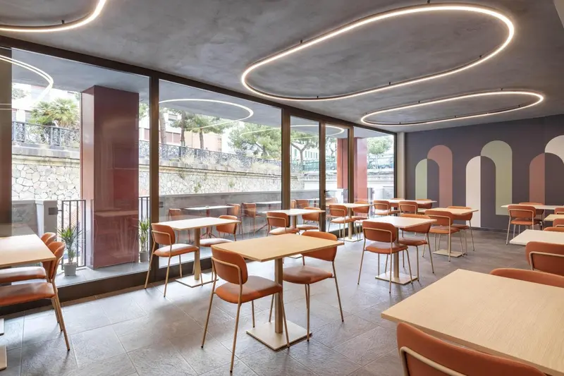 Une salle lumineuse avec des tables et des chaises oranges près de grandes fenêtres.