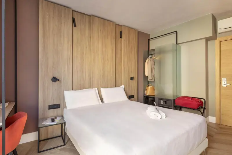 Une chambre moderne avec un grand lit blanc et des murs aux tons neutres.