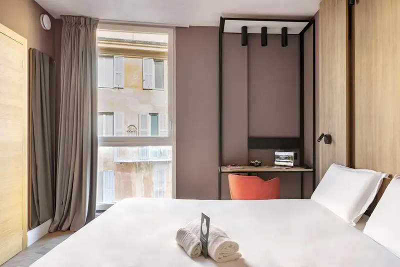 Une chambre lumineuse avec un lit blanc et un bureau rouge.