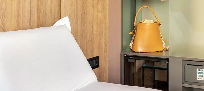 Un lit blanc avec un oreiller moelleux et un sac en cuir marron sur une table de chevet.