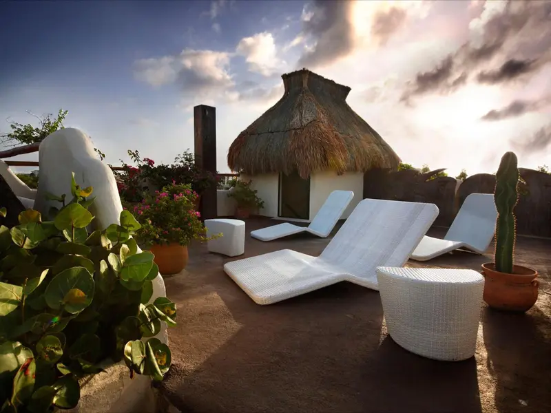 Terrasse aménagée avec chaises longues et végétation tropicale au coucher du soleil.